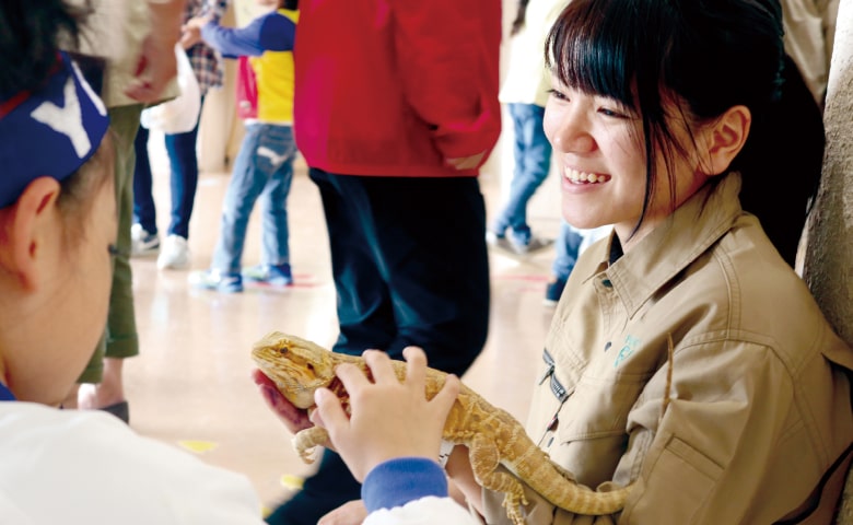爬虫類を手に乗せた女性と、その爬虫類を撫でる子ども