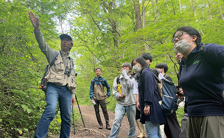森の中を案内する男性と、説明を聞く学生たち
