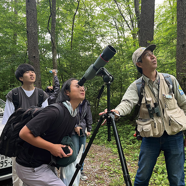 森の中で望遠鏡をのぞく学生