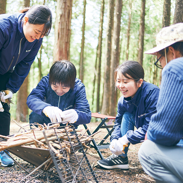 森の中で焚火の用意をする学生たちと先生